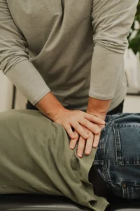 Close-up of a person's hands, wearing a gold ring, pressing on the lower back of another person wearing olive green pants and blue jeans.