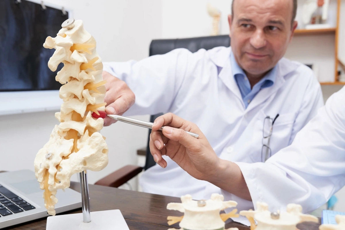 A doctor and another person pointing at a herniated disc on a human spine model with a pen.