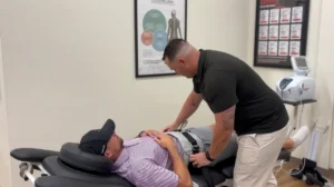 A practitioner in a black shirt adjusts a grey harness on a patient lying on a chiropractic table.